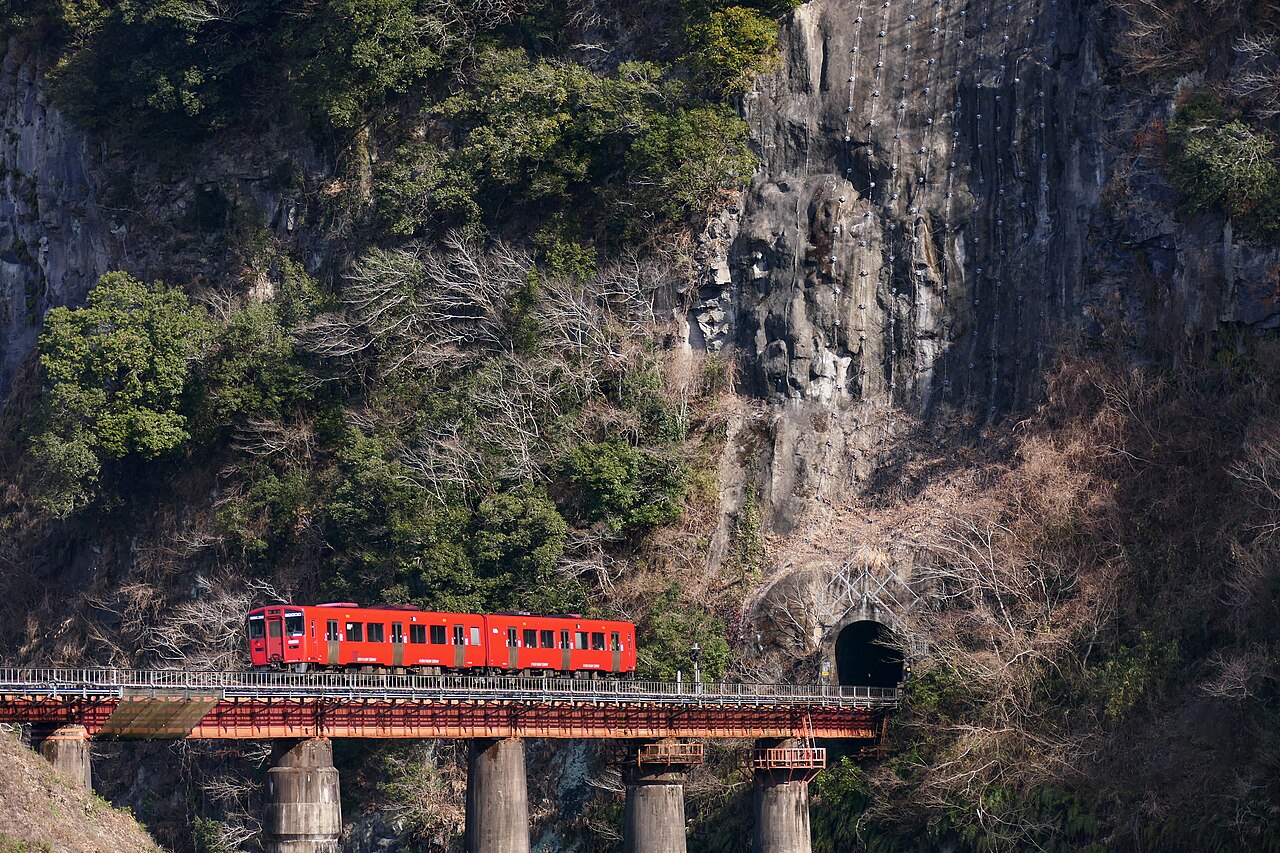 A Kiha 200 series train on the Hōhi Main Line passing the Iwado cliffs of the Bungo-Ōno Geopark.