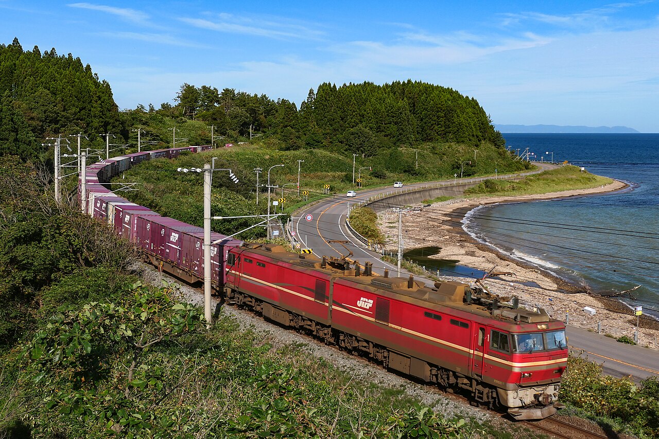 JR Freight Class EH800 No. 11 hauling a container freight train, with the Tsugaru Strait behind, on the Donan Isaribi Railway Line.