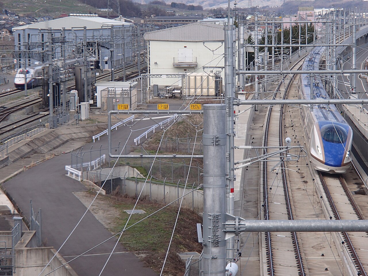 An E7 series set running a "Hakutaka" No. 566 service past a depot on the Hokuriku Shinkansen.